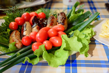 Grilled sausages with tomatoes and onions on large plate.