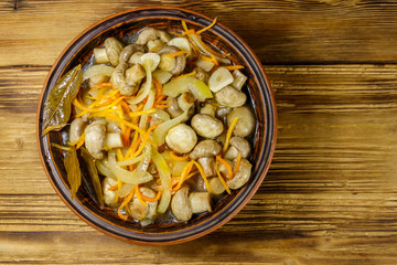 Delicious marinated mushrooms with carrot, onion and spices in ceramic bowl on wooden table. Top view