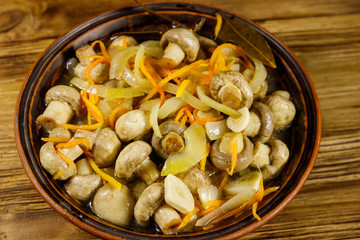 Delicious marinated mushrooms with carrot, onion and spices in ceramic bowl on wooden table