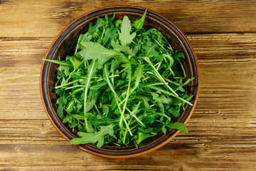 Fresh green arugula in ceramic bowl on a wooden table. Top view. Healthy food or vegetarian concept