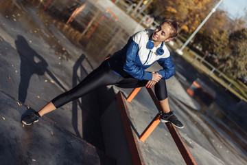 Obraz premium Fit slim woman in sportswear and headphones practicing leg stretching before training in a sports park