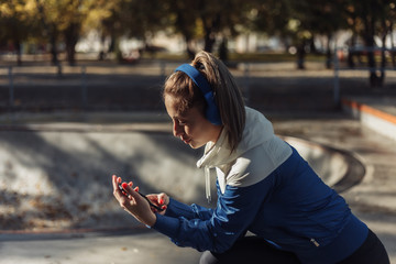 Young attractive sport woman in sportswear with headphones listens to music at sports park.