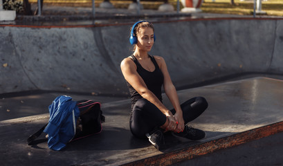 Fototapeta na wymiar Attractive fit woman in sportswear listens to music with headphones while sitting in sports park