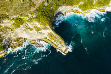 View from above, stunning aerial view of a green limestone cliff bathed by a turquoise sea during sunset. Nusa Penida, Indonesia. Nusa Penida is an island southeast of Bali, Indonesia.