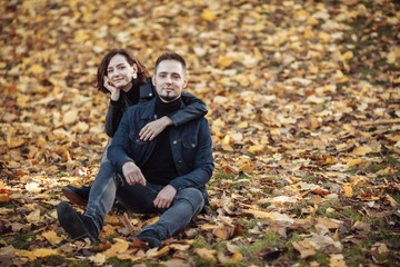 Naklejka na ściany i meble Young hugging couple of lovers on a blurry background of fallen autumn leaves in the park. Romantic, love concept