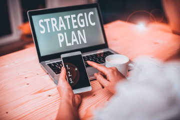 Text sign showing Strategic Plan. Business photo text a systematic process of envisioning a desired future woman laptop computer smartphone mug office supplies technological devices