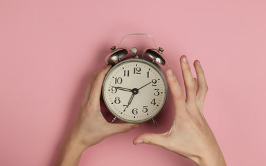 Creative flat lay morning time emotions concept. Angry female hand holds retro alarm clock on pink...