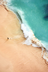Stunning aerial view of a person running on a beautiful beach bathed by a turquoise sea during sunset. Kelingking beach, Nusa Penida, Indonesia. Nusa Penida is an island southeast of Bali, Indonesia.