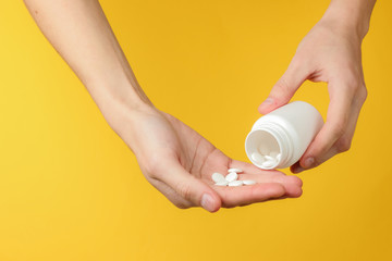 Female hands is holding white pill bottle and pills on yellow background. Health. Disease.
