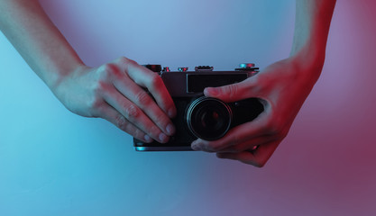 Female hands hold a retro camera. Creative pop art pink blue neon color. Trendy gradient illumination. Night light
