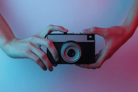 Female hands hold a retro camera. Creative pop art pink blue neon color. Trendy gradient illumination. Night light