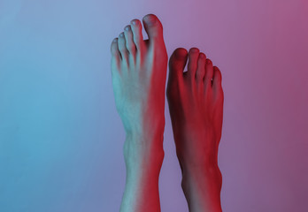 Barefooted female legs close-up. Creative pop art pink blue neon color. Trendy gradient illumination. Night light