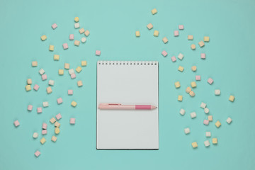 Notebook with pen and lot of marshmallows on blue pastel background. Top view