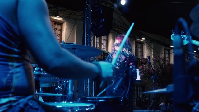 Camera moving from botton to the top, in slow motion pointed at drummer's hands playing a song in an outdoor concert