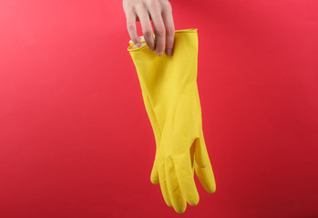 Female hand hold yellow gloves for cleaning on a red background. Home cleaning concept