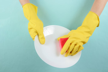 The concept of a housewife washing dishes. Hands in yellow latex gloves wash the plate with sponge on blue background