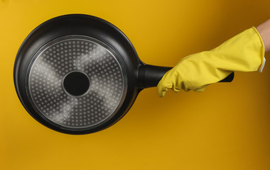 Hand in a rubber glove holds non-stick pan on yellow background.