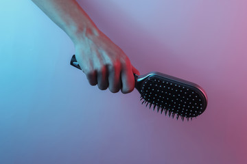 Hand holds hair comb. Creative pop art pink blue neon color. Trendy gradient illumination. Night...