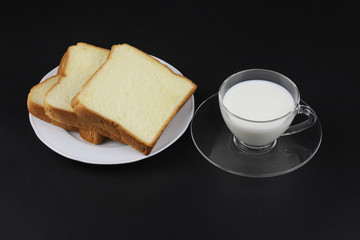 Sliced bread on white plate with cup of milk on black background