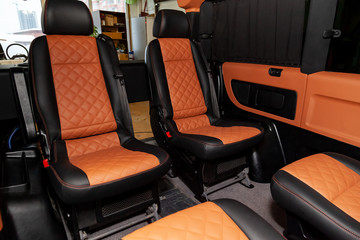Four rear seats in a minibus are deployed to each other and tightened in black and brown leather with a diamond-shaped stitching thread in a workshop for tuning and repairing vehicles. Van car.