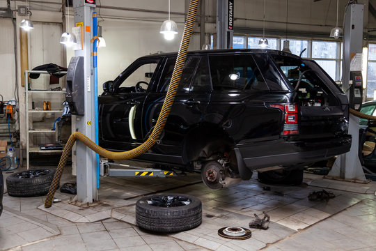 Used black car Land Rover Range Rover disassembled without bumper and wheels on a four-post lift for repairing the chassis and engine in a vehicle repair workshop