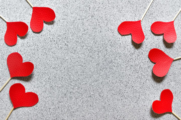 Many red fabric cloth hearts on wooden sticks on gray stone like texture background arranged along the border. Photo with copy blank space.