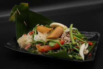 Spicy salad with sausage, mushroom and vegetables on banana leaf in lack plate