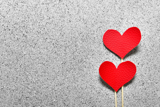 Two red fabric cloth hearts on wooden sticks on gray stone like texture background. Photo with copy blank space.