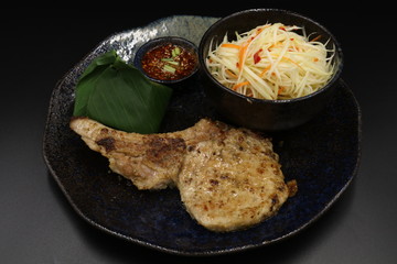 Grilled pork chop black pepper steak with somtum and Tha ispicy sauce on black plate