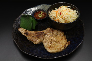 Grilled pork chop black pepper steak with somtum and Tha ispicy sauce on black plate