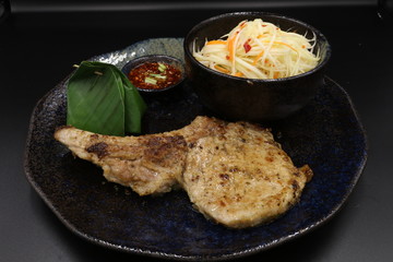 Grilled pork chop black pepper steak with somtum and Tha ispicy sauce on black plate