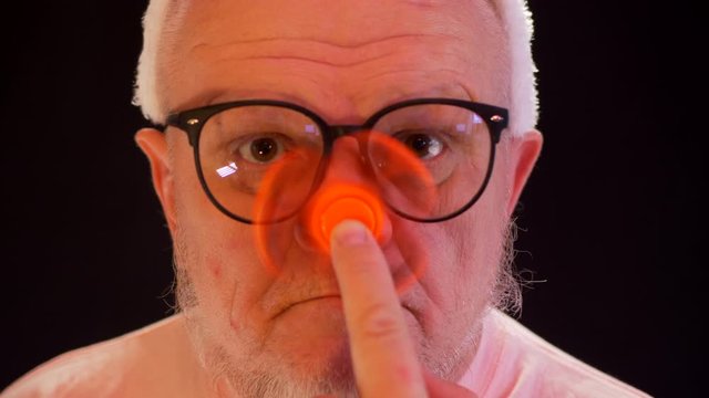 Portrait of a strange elderly man who twists spinner on his nose. Freaky senior citizen spinning with gray beard and big glasses. bizarre men with orange spinner