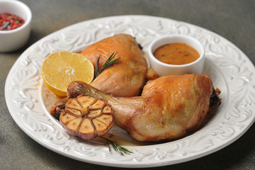 Chicken leg on a plate.  Drumstick served with green salad, sauce, lemon and grilled garlic. Gray background. Close-up. 