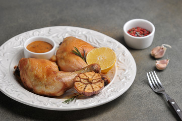 Chicken leg on a plate. Drumstick served with green salad, sauce, lemon and grilled garlic. Gray background. Close-up. Macro shot.