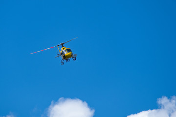 Fototapeta na wymiar Elicottero giallo in volo su un cielo blu intenso con qualche nuvola. Copy space. Utilizzato per interventi di salvataggio in montagna