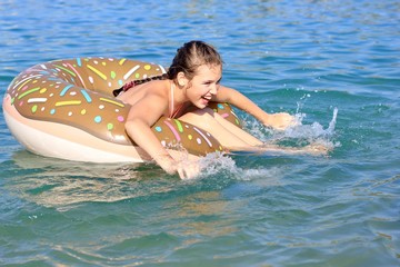 Teen girl swims on a circle in the sea. Inflatable toy, swimming circle in the form of a chocolate donut. 