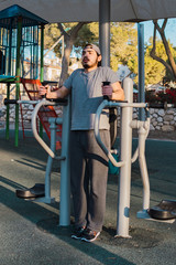 young man exercising abdomen and legs in public park equipment.