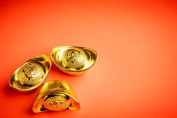 Chinese gold bars against red background. The wordings on bar is chinese words which means “bring in wealth and treasure”