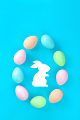 Multicolored dyed handmade pastel easter eggs form egg shape with white bunny in the middle on blue background in flat lay with copy space. Happy Ester greeting card