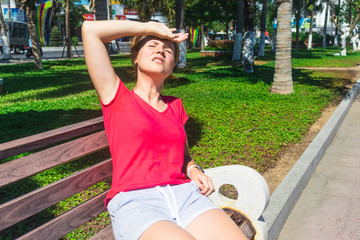 Girl sitting on the bench, suffering from heat, woman with heatstroke. Having sunstroke at summer...