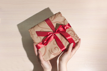  Gift with a red ribbon on a light background in female hands. The concept of sales, purchases, Christmas holidays and birthday. View from above.