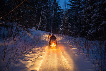 snowmobile in the evening goes through the winter forest. headlights. night road through the winter...