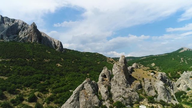 Top view of the mountains, the valley, the road and the forest on a cloudy day. Shot. Flying over the stone rocks and green vegetation growing on hill slopes.
