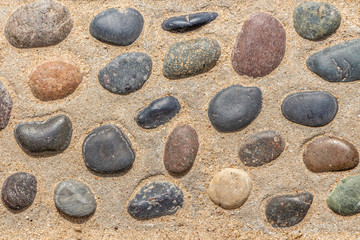 Fototapeta na wymiar Beautiful texture of path of gray and color smooth stones on the yellow background with sand is in the park