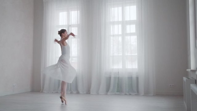ballet dancer is spinning on tiptoe in a snow-white dress in a bright studio on the background of large windows