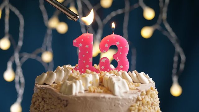 Birthday cake with 13 number pink candle on blue backgraund. Candles are set on fire. Slow motion and close-up view