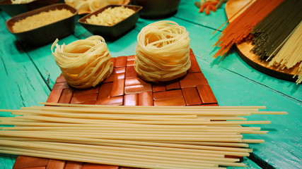Dry spaghetti and nest pasta lie on board. Close Up.  Spaghetti and two nest pasta are on eco-friendly wooden table next to other pasta.