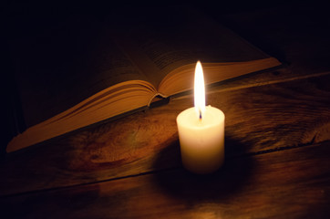 burning candle and a book on a table in the dark on a wooden table. Concept of knowledge, religion, magic