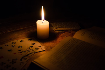 mystical atmosphere, cards, a book, a lighted candle in the dark on a wooden table. Esoteric concept, fortune telling and predictions