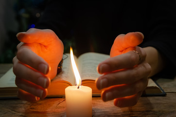 Hands near the candle and a book on the table. Concept of magic, education